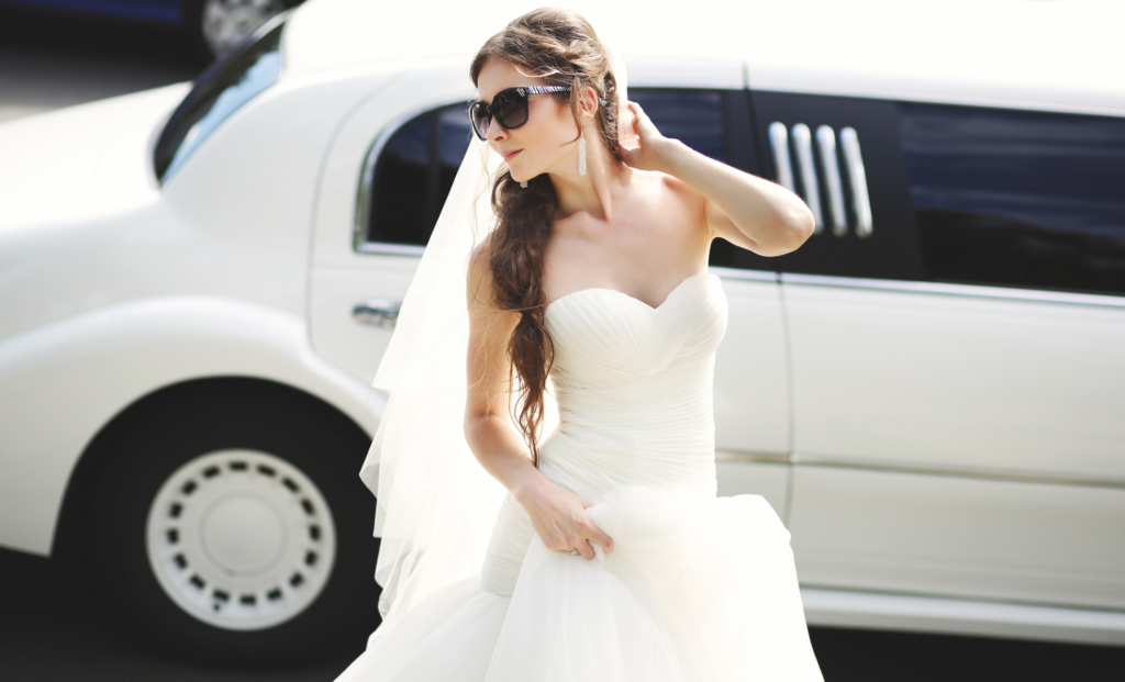 Bride in a wedding gown posing beside a white stretch limousine
