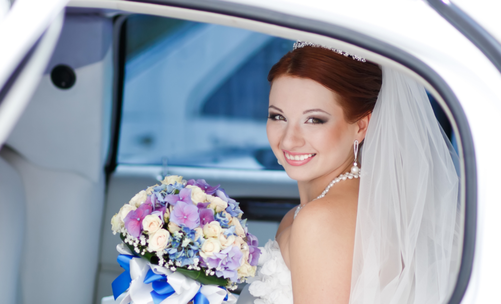 Smiling bride with her bouquet in the window of a white wedding car
