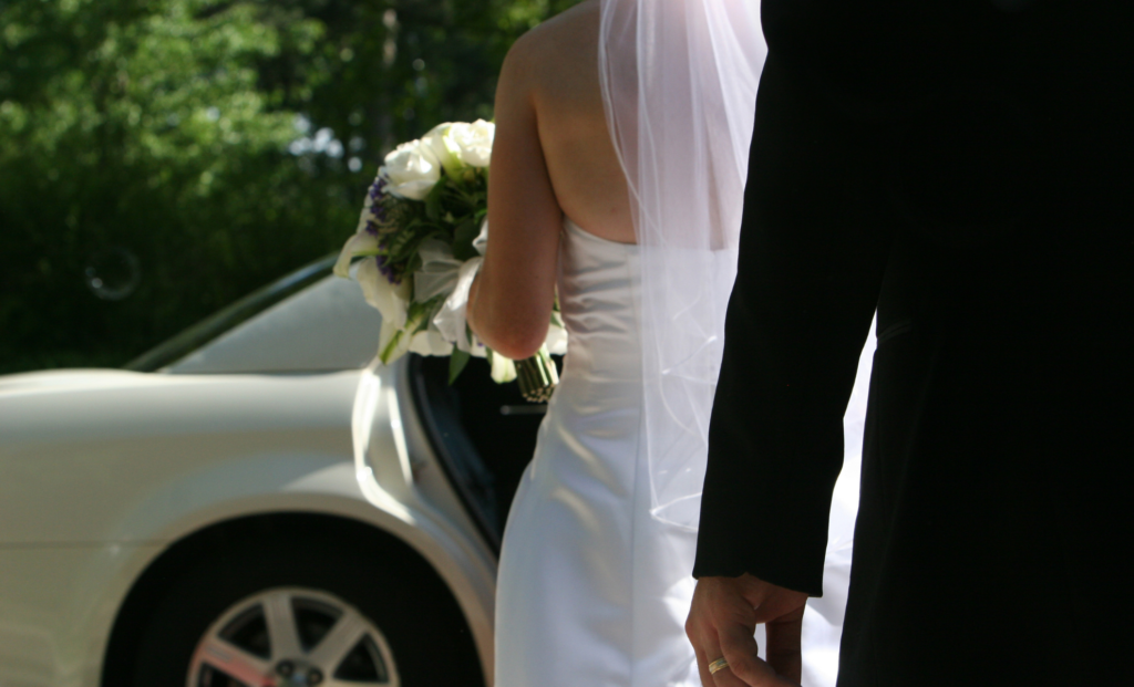Bride and groom holding hands beside a wedding limousine