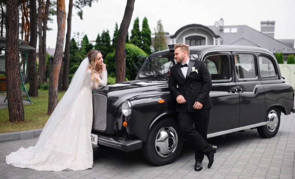 Bride and groom posing beside a classic black vintage car